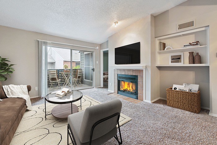 Cozy living room with plush carpeting, modern fireplace, and access to a charming outdoor patio through sliding glass doors. Elegant furnishings and a serene atmosphere.