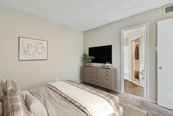 Cozy bedroom with stylish decor, featuring a comfortable bed, modern dresser, and a sleek TV. The room is enhanced with soft lighting and an art piece on the wall, leading to an elegant en-suite bathroom.