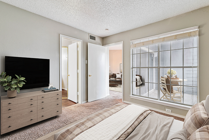 Inviting bedroom with cozy carpeting, elegant dresser, and expansive window view leading to a bright outdoor seating area.
