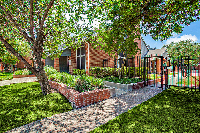 Charming apartment building with a red brick exterior, surrounded by lush greenery and a secure gated entrance.