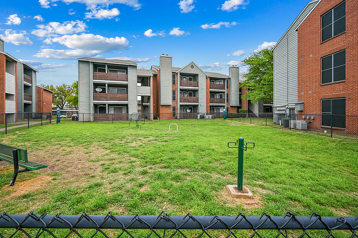 Charming dog park surrounded by red-brick apartment building, lush greenery.
