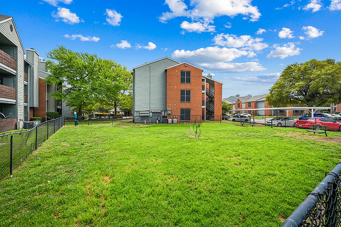 Charming dog park surrounded by red-brick apartment building, lush greenery.