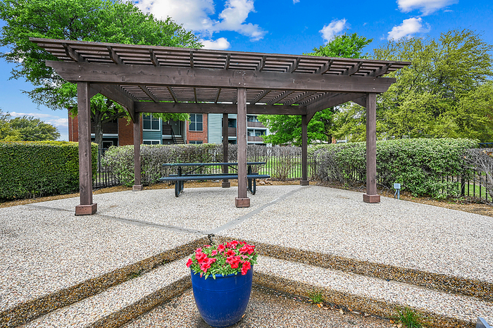 Charming outdoor patio with wooden pergola and picnic bench, surrounded by lush greenery and vibrant flowers, perfect for relaxation.