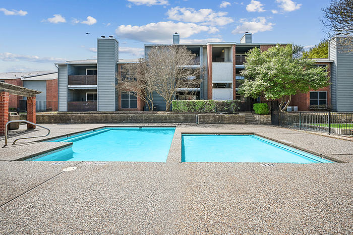 Inviting outdoor pool area of a modern apartment complex featuring azure blue swimming pools under a clear sky, surrounded by lush greenery and elegant architecture.