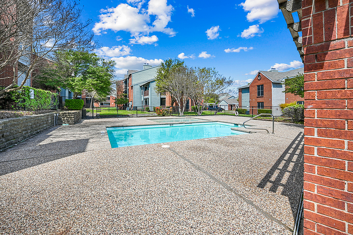 Inviting outdoor pool area surrounded by lush greenery and modern apartment buildings under a bright blue sky.