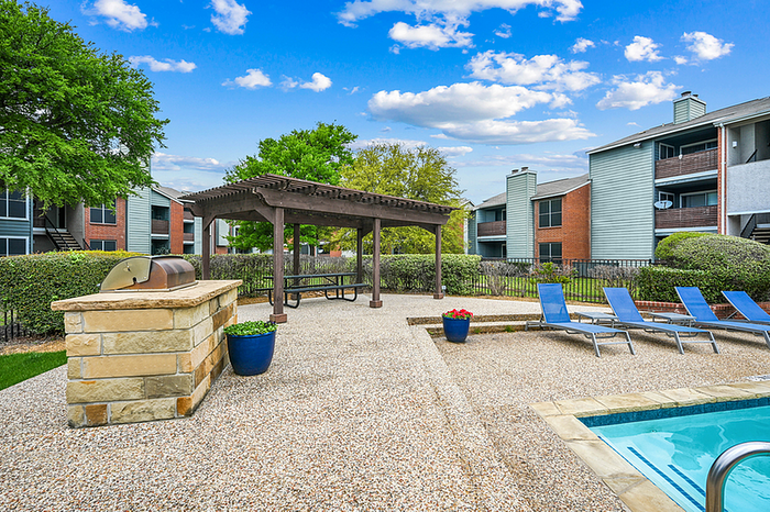 Chic outdoor apartment amenities featuring a pergola-shaded picnic area, modern grill, inviting pool, and stylish lounge chairs surrounded by lush greenery and vibrant architecture.