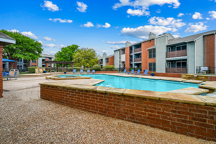 Charming apartment community with a sparkling outdoor pool, surrounded by lush greenery and modern architecture under a bright blue sky.