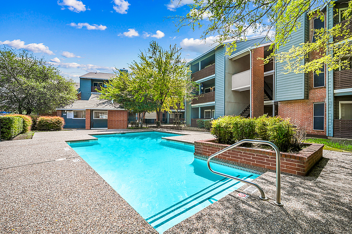 Contemporary apartment community with inviting outdoor pool, lush greenery, and brick accents under a bright blue sky.