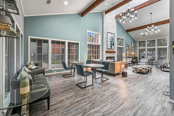 Inviting and stylish apartment clubhouse featuring elegant chandeliers, large windows for natural light, and a cozy fireplace with modern seating.