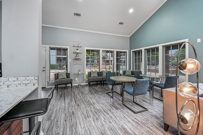 Modern clubhouse featuring sleek wood flooring, cozy seating arrangements, and abundant natural light through large windows, ideal for relaxation and socializing.