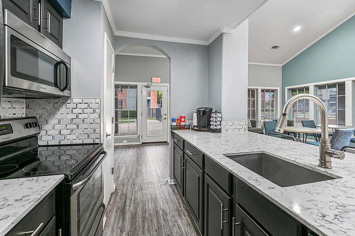 Modern clubhouse kitchen with sleek appliances, elegant marble countertops, and a spacious open layout leading to a bright dining area.