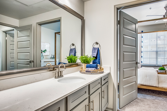 Bright and modern bathroom featuring a sleek vanity with dual sinks, elegant fixtures, and a view into a cozy bedroom filled with natural light.