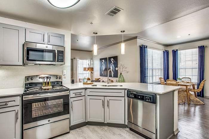 Modern kitchen with sleek stainless steel appliances, elegant cabinetry, and a bright dining area featuring large windows and stylish decor.