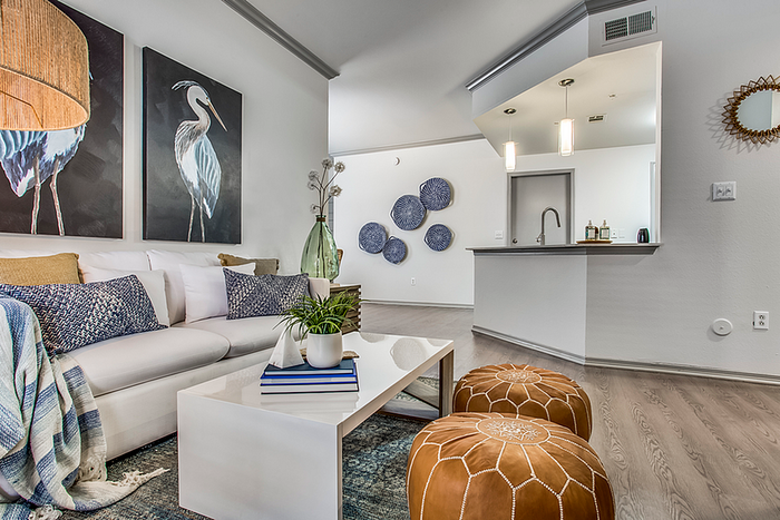 Chic living room with modern decor, featuring a cozy white sofa, stylish cushions, vibrant artwork, and a sleek open kitchen in the background.