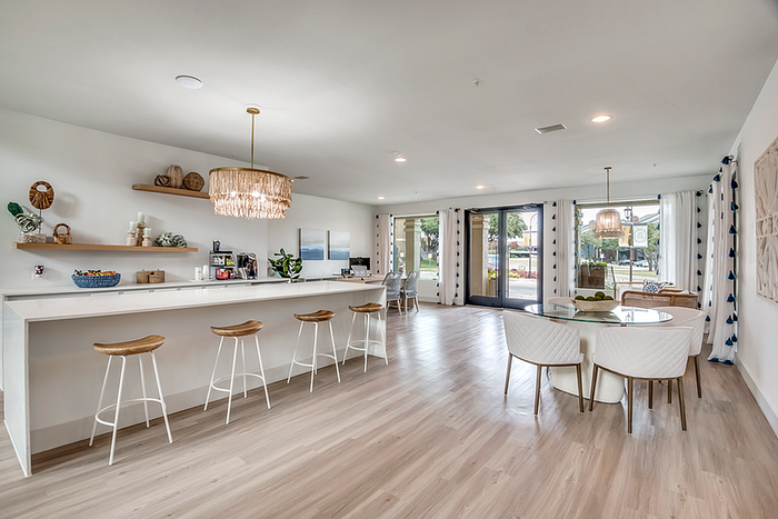 Bright, open-concept living space with a sleek modern kitchen, elegant lighting fixtures, and a spacious dining area overlooking lush greenery.