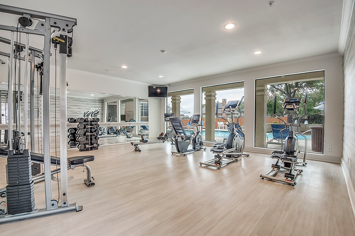 Modern fitness center featuring state-of-the-art exercise equipment, large mirrors, and pool views through expansive windows.