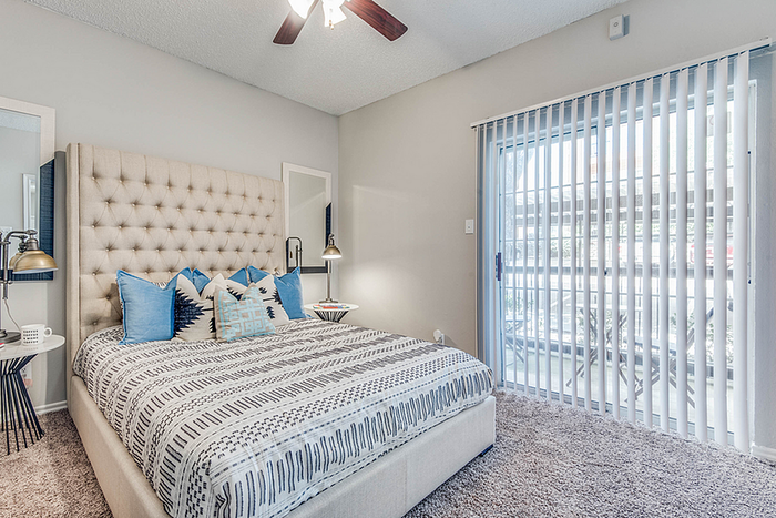Inviting bedroom featuring a plush, tufted bed with stylish pillows, cozy carpet, and sliding glass doors leading to outdoor views.