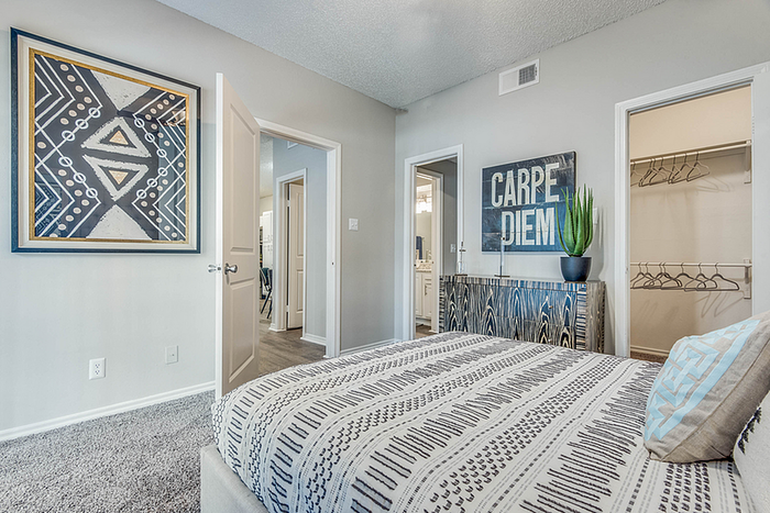 Inviting bedroom in a modern apartment, featuring a patterned bedspread, geometric wall art, and an open walk-in closet.