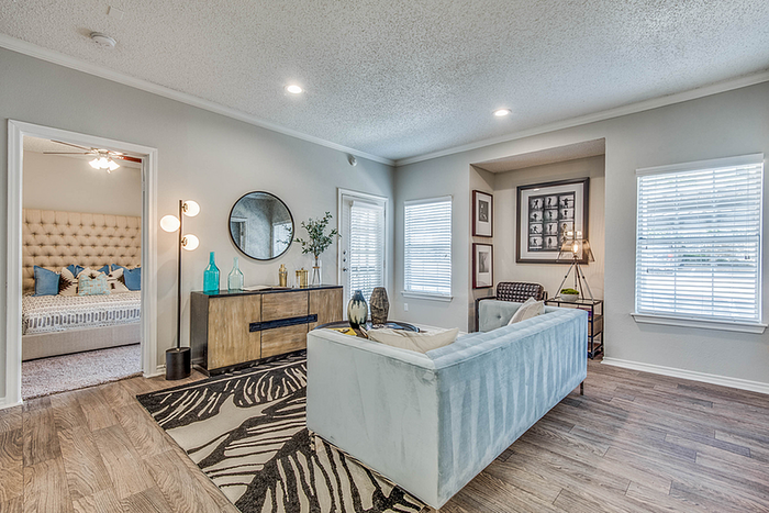 Inviting living room with stylish decor, featuring plush seating, elegant wooden flooring, and abundant natural light, adjacent to a cozy, well-appointed bedroom.