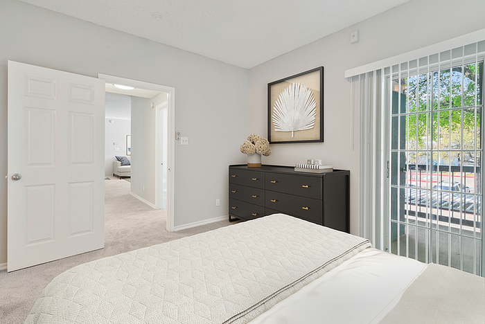Bright bedroom with modern decor, featuring a cozy bed, sleek dresser, and sliding glass doors opening to a serene outdoor view.