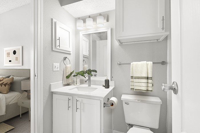 Bright white bathroom with modern fixtures, a sleek vanity, and a glimpse of an elegantly styled bedroom, embodying contemporary comfort.
