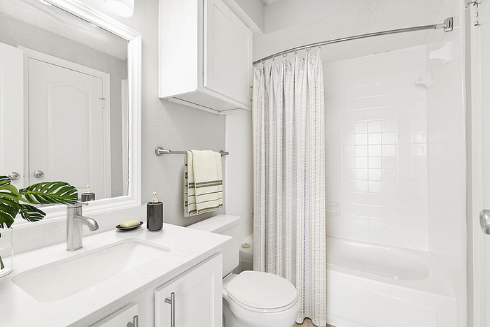 Bright and modern bathroom featuring a sleek white vanity, spacious mirror, and elegant tiled shower with a curved curtain rod.