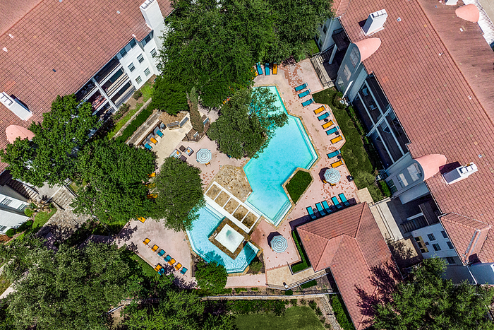 Aerial view of a modern apartment community with a beautifully landscaped pool area surrounded by lush greenery and stylish lounge chairs.