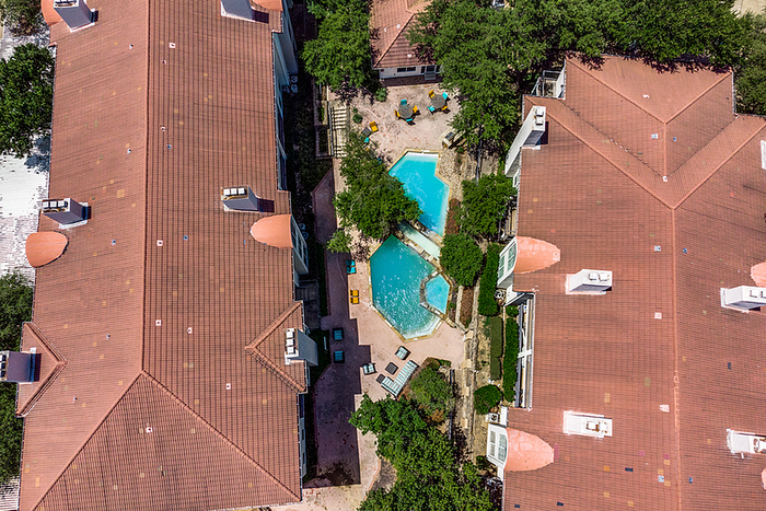Aerial view of apartment community with terracotta roofs, lush greenery, and a central sparkling pool surrounded by sun loungers.