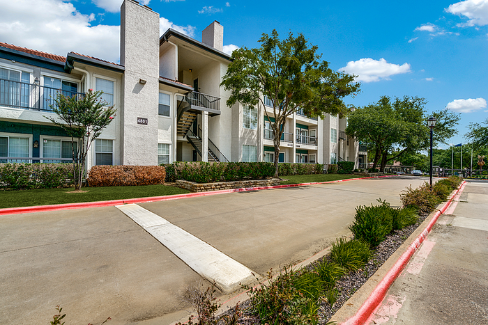 Charming mid-rise apartment building with modern design, set amidst lush greenery and blue skies.