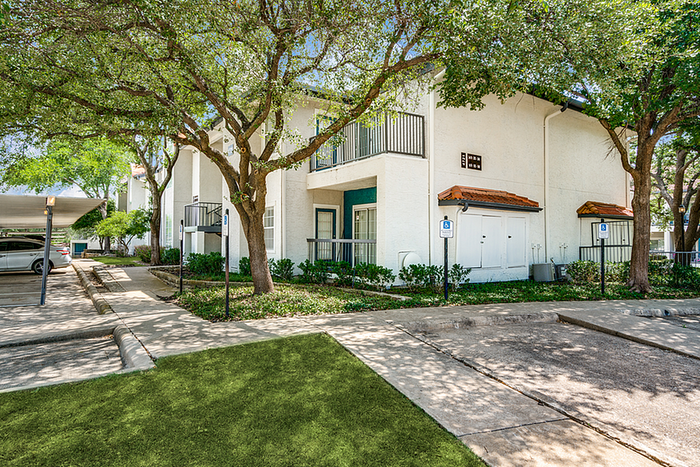 Charming apartment community with lush greenery, shaded parking, and inviting balconies, offering a serene and inviting living environment.