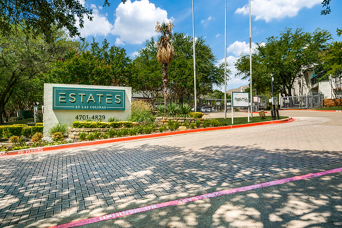 Inviting entrance of Estates at Las Colinas, surrounded by lush greenery and vibrant landscaping, showcasing modern living.