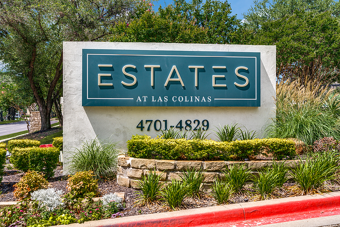Inviting entrance to Estates at Las Colinas, featuring vibrant landscaping and a prominent address display.