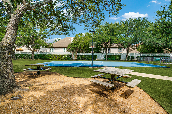 Inviting outdoor area featuring a basketball court, surrounded by lush greenery, with picnic tables for relaxation and enjoyment.