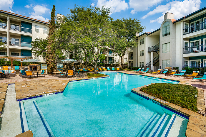 Elegant apartment community featuring a pristine swimming pool, lush greenery, and ample poolside seating, perfect for relaxation and leisure.