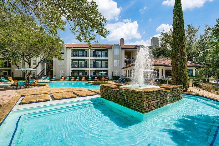 Inviting apartment community with a beautifully landscaped pool area, vibrant outdoor seating, and charming architecture under a clear blue sky.