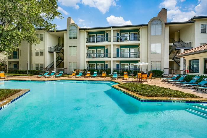 Luxurious apartment community with a swimming pool, inviting lounge chairs, and lush landscaping under a clear blue sky.