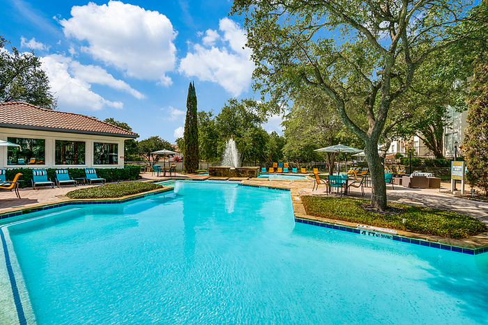 Inviting swimming pool area with lounge chairs, lush greenery, and a serene fountain under a bright blue sky.