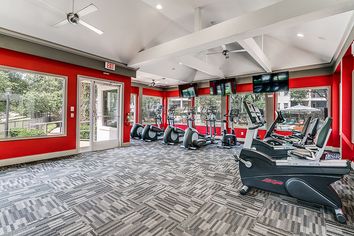 Bright and modern fitness center with vibrant red walls, equipped with treadmills and exercise bikes, offering scenic outdoor views.