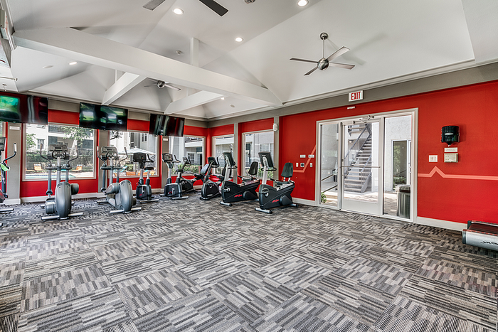 Modern fitness center featuring state-of-the-art cardio machines, vibrant red walls, and ample natural light.