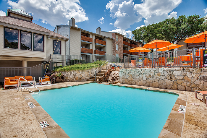 Inviting apartment pool area with vibrant orange umbrellas, cozy seating, and scenic landscape for ultimate relaxation.