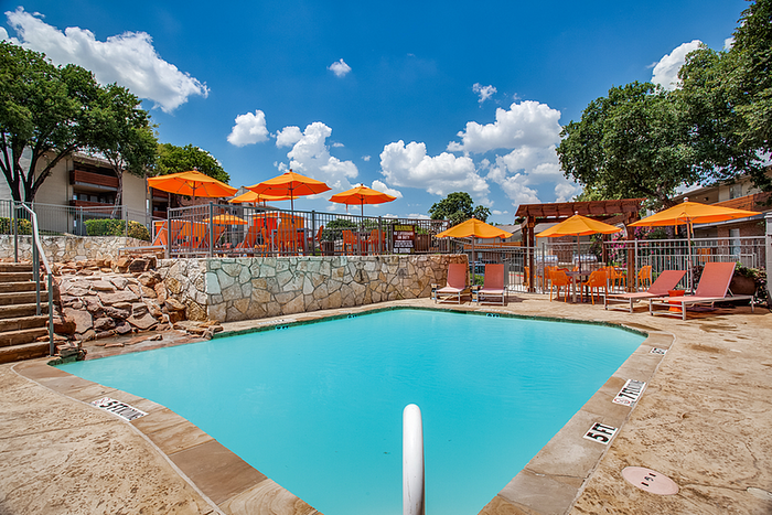 Inviting outdoor pool area with bright orange umbrellas and comfortable lounge chairs, set against a picturesque blue sky.