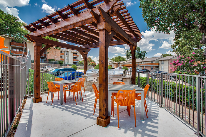 Charming outdoor patio with wooden pergola, modern grill, and vibrant orange seating, ideal for entertaining and enjoying sunny days.