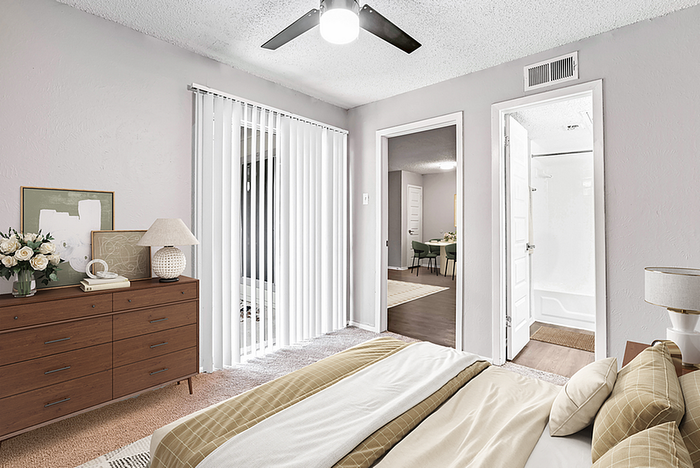 Elegant bedroom with modern decor, featuring a cozy bed, stylish dresser with decorative accents, and abundant natural light from vertical blinds. Access to a sleek bathroom and inviting dining area adds convenience and charm.