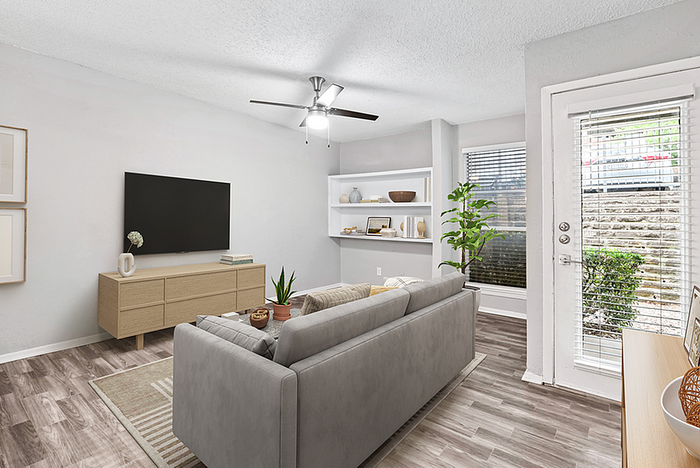 Bright and modern living room featuring elegant hardwood floors, a cozy gray sofa, large wall-mounted TV, and natural light streaming through wide windows.