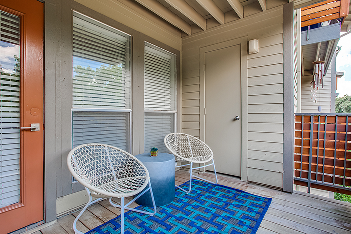 Charming apartment balcony with cozy seating, bright blue rug, and warm natural light.