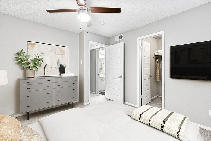 Modern bedroom featuring a sleek dresser, stylish artwork, integrated closet, and a mounted flat-screen TV.