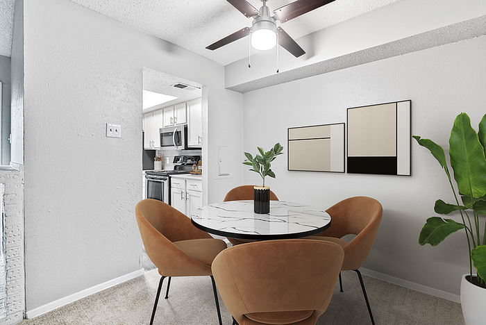 Chic dining area with a round marble table, elegant chairs, and contemporary wall art, next to a modern kitchen.