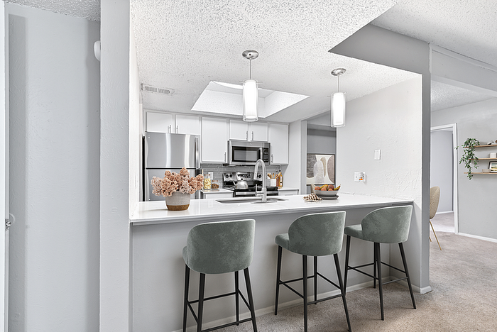 Contemporary open-plan kitchen with sleek white cabinetry, stainless steel appliances, and elegant pendant lighting over a stylish breakfast bar with plush seating.