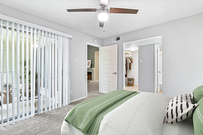 Bright bedroom with modern green accents, ceiling fan, and sliding glass doors leading to a private balcony.