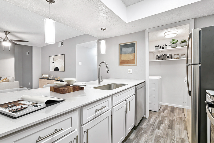 Modern open-concept kitchen with sleek white cabinetry, stainless steel appliances, and stylish wood flooring adjacent to a cozy living area.